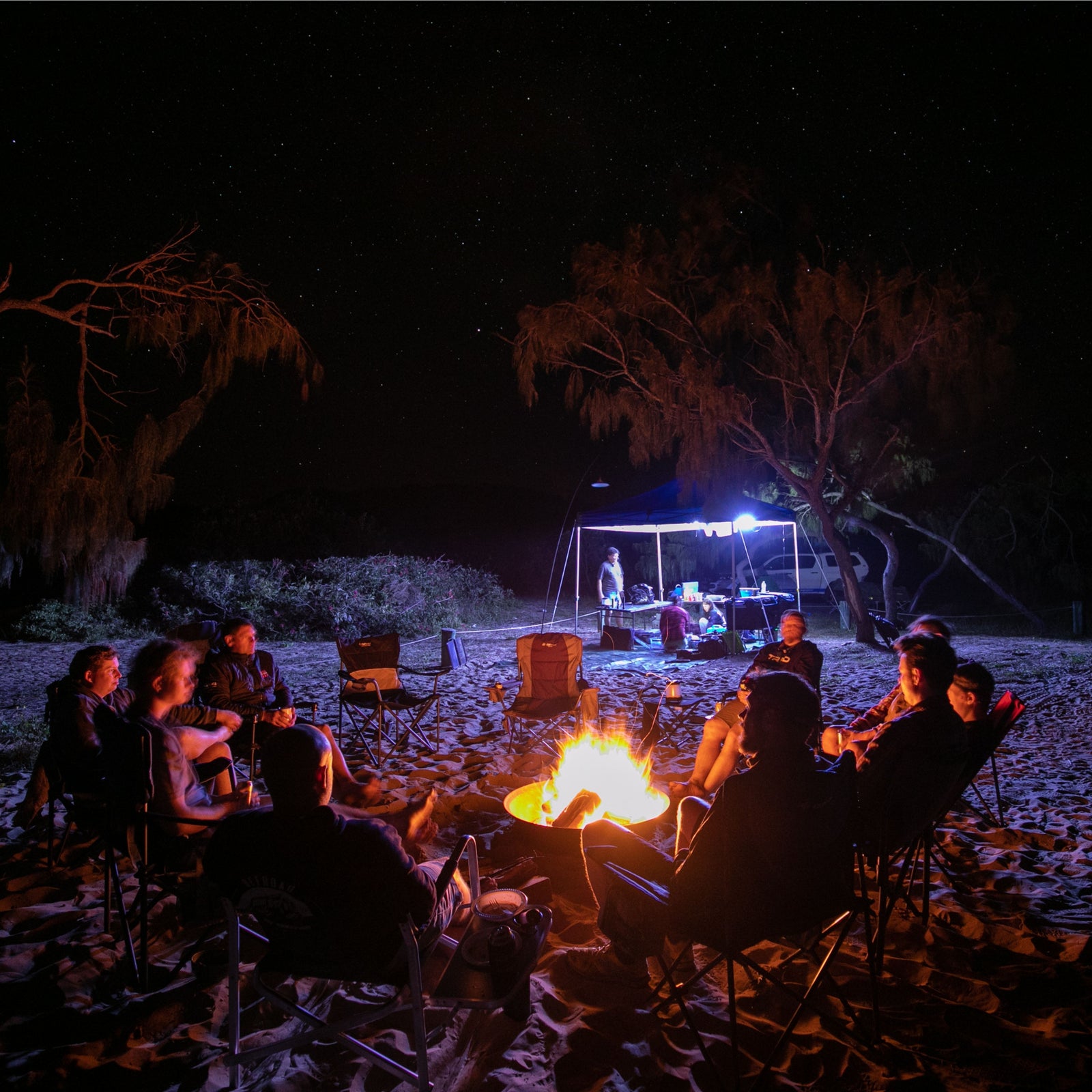 People sitting on beach around campfire made without matches